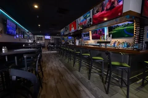 Empty modern bar with multiple TVs, blue lights, and wooden finishes.