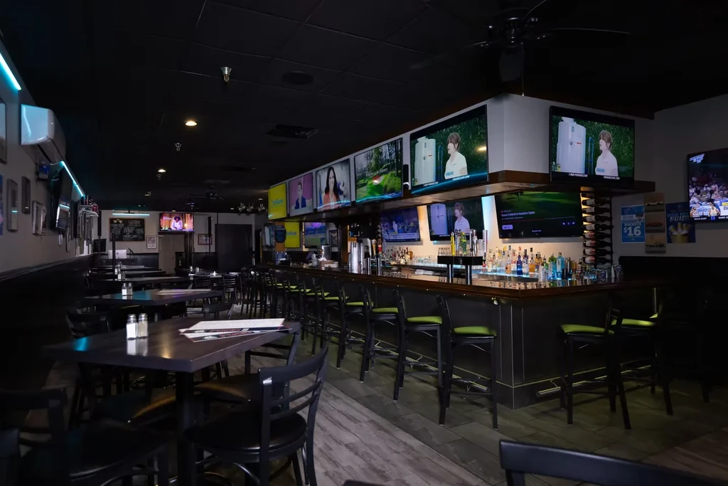 Modern sports bar: dining tables, green bar stools, multiple TVs.