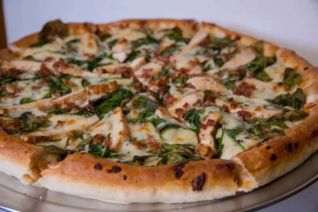 Close-up of sliced pizza with cheese, chicken, spinach, and bacon.