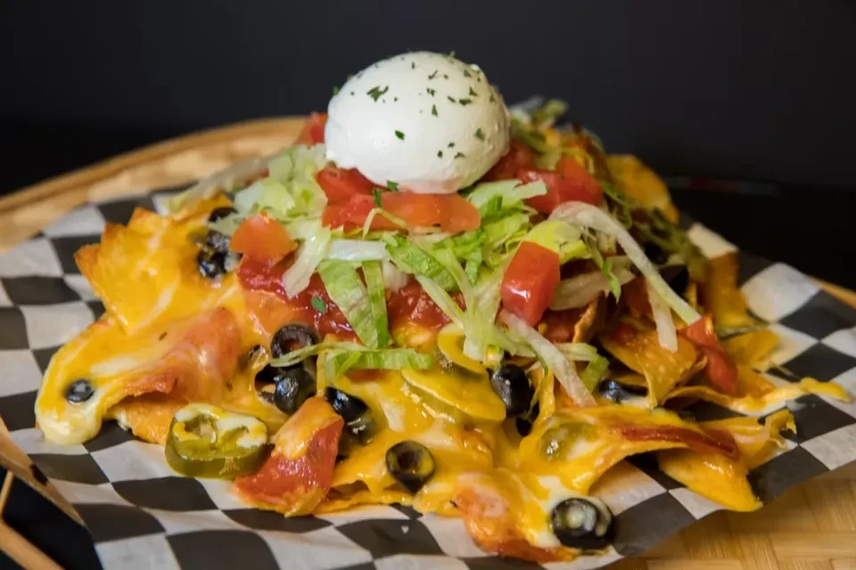 Loaded nachos with melted cheese, jalapeños, olives, sour cream, lettuce, tomatoes.