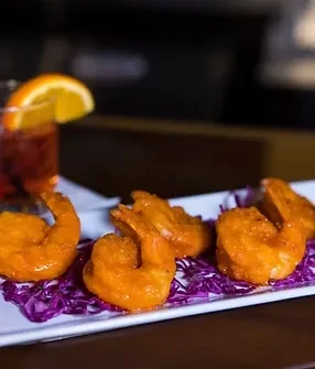 Four fried shrimp on red cabbage with a garnished drink.