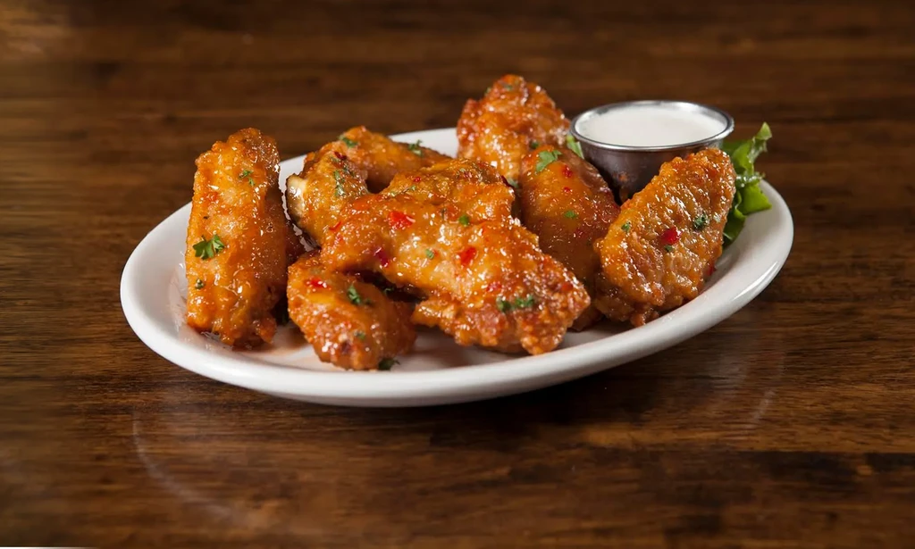 Shiny glazed chicken wings with chili flakes, herbs, and dipping sauce.