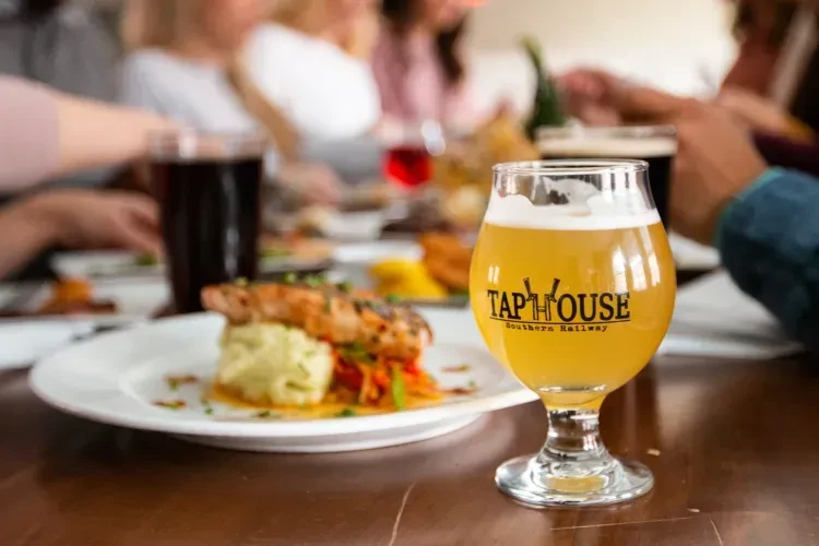 Grilled fish dish and frothy beer with "TAP HOUSE" logo.
