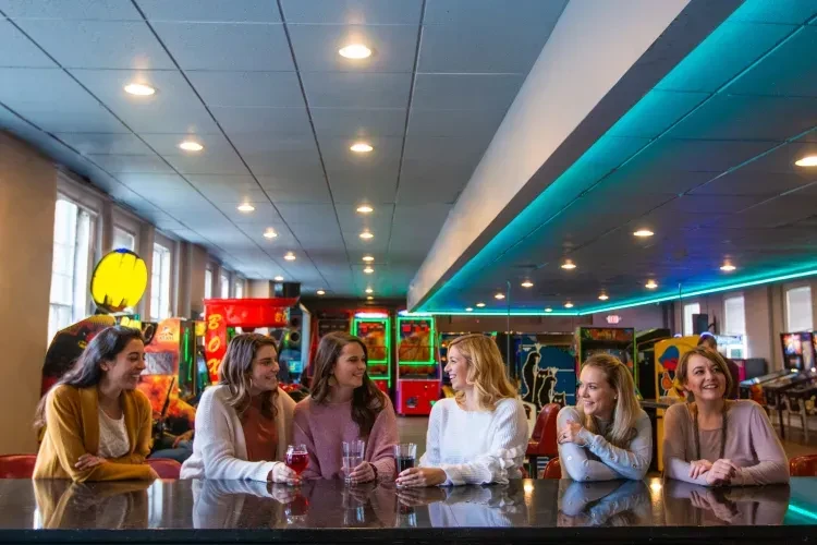 Six women talking and laughing at an arcade bar.