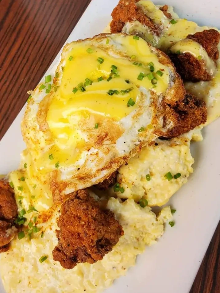 Overhead: Fried chicken, sunny-side eggs, and sauce on creamy grits.