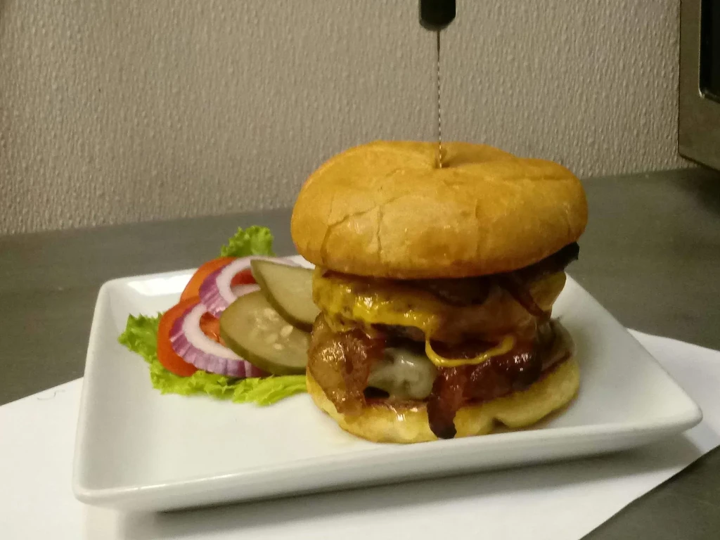Gourmet burger with bacon, cheese, and pickles on a white plate.
