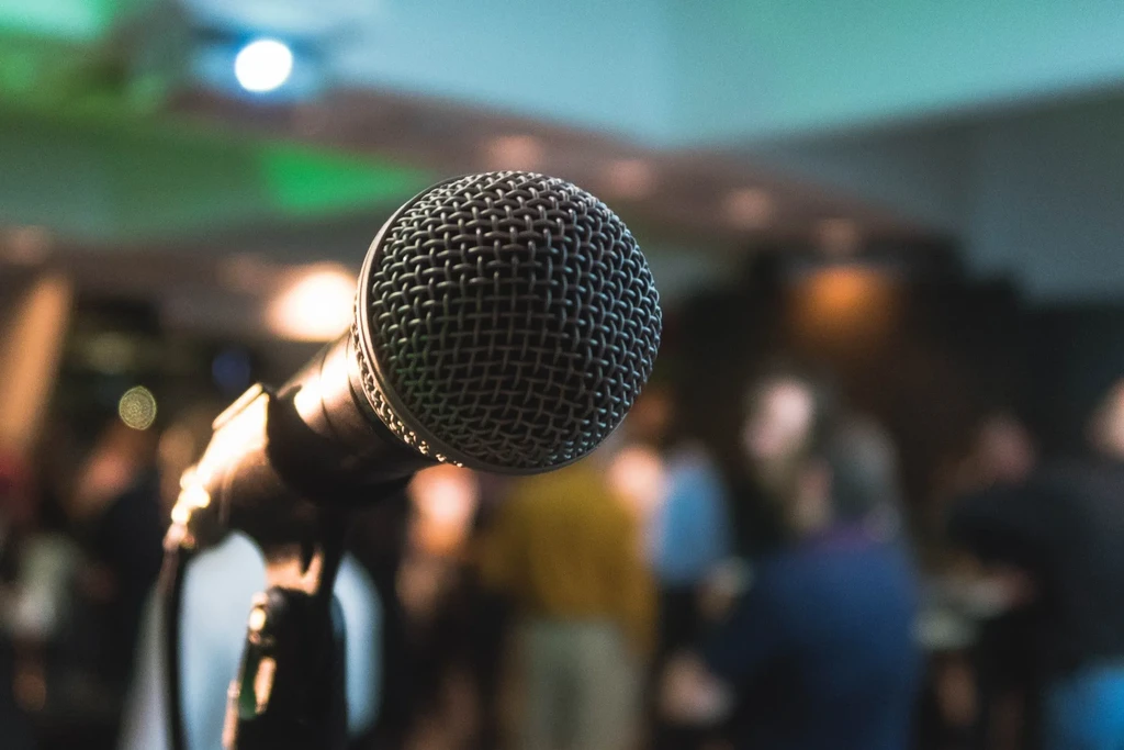 Close-up black vocal microphone, blurred crowd, colorful stage lights.