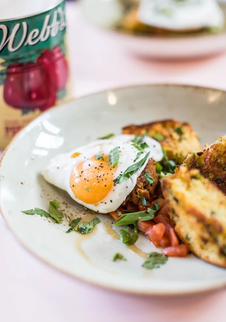 Fried egg, tomatoes, and corn fritters on a beige rustic plate.