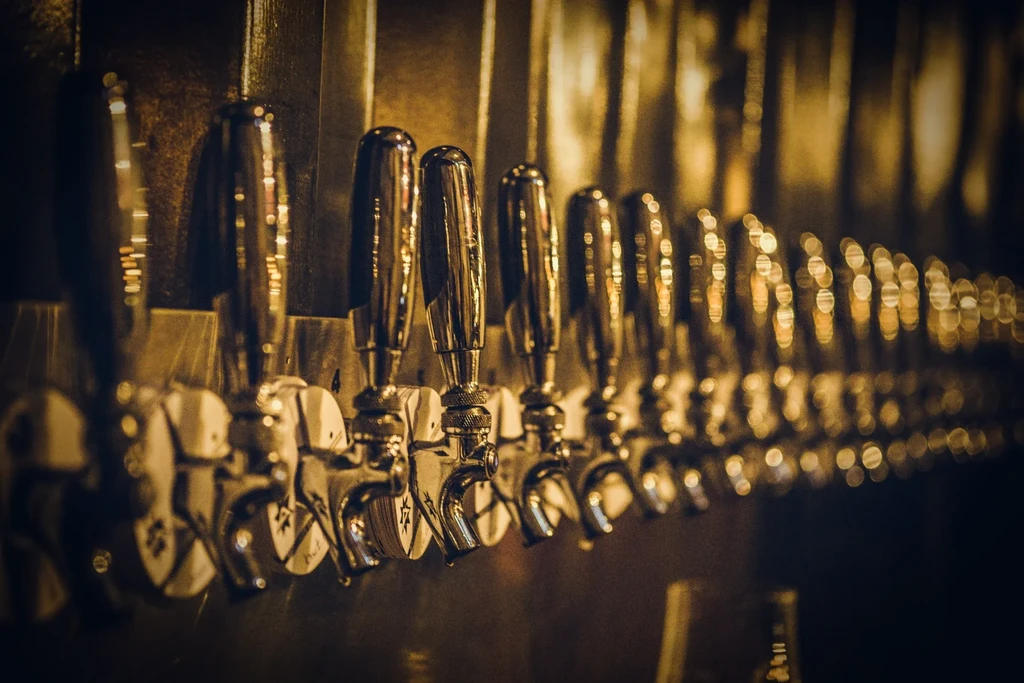 Close-up of many glowing, metallic beer tap handles in warm light.