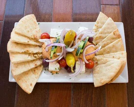 Hummus with various toppings and pita bread on a white platter.