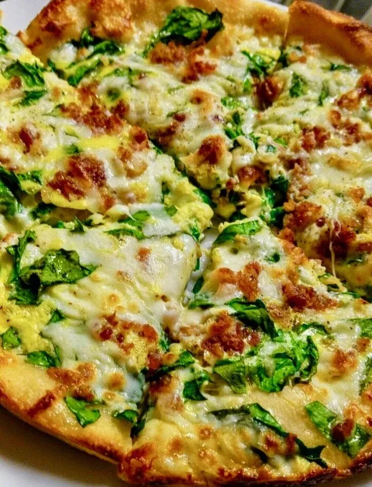 Pre-cut pizza with melted cheese, leafy greens, and crumbled meat.