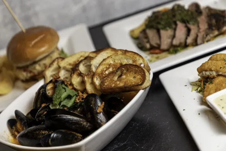 Mussels, burger, fried food, and steak dishes on a dark tabletop.