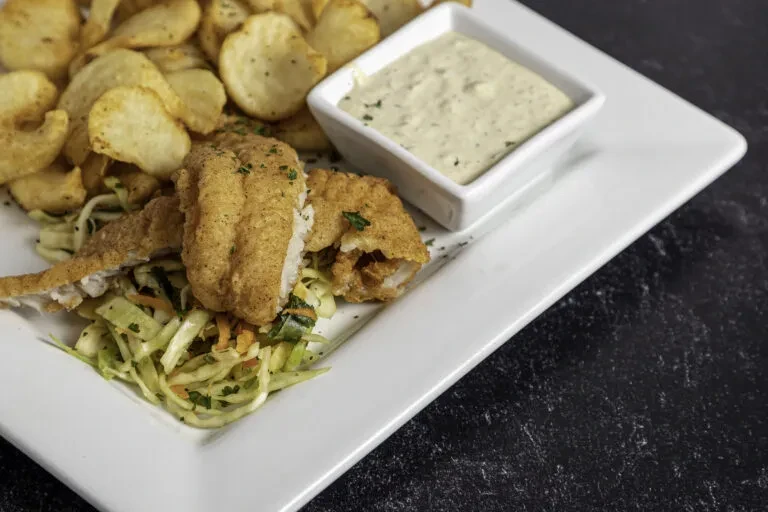 A plate of fried fish, chips, coleslaw, and dipping sauce.