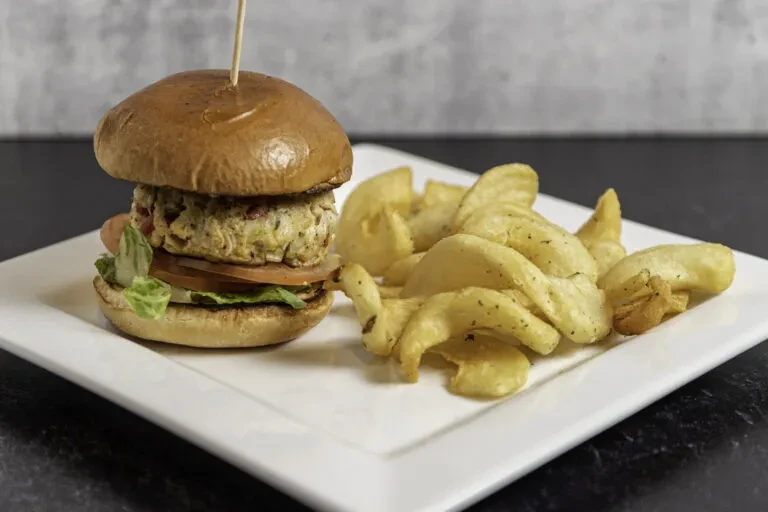 Slider, potato wedges, tomato, and lettuce on a white rectangular plate.