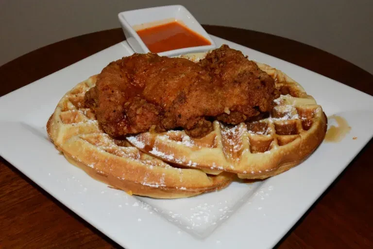 Crispy fried chicken on waffles with powdered sugar, syrup, and side sauce.