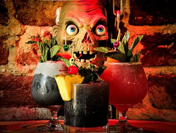 Three elaborately garnished cocktails with a grotesque zombie head.