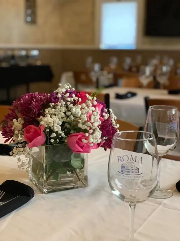 Restaurant table with floral centerpiece and Roma Ristorante wine glass.