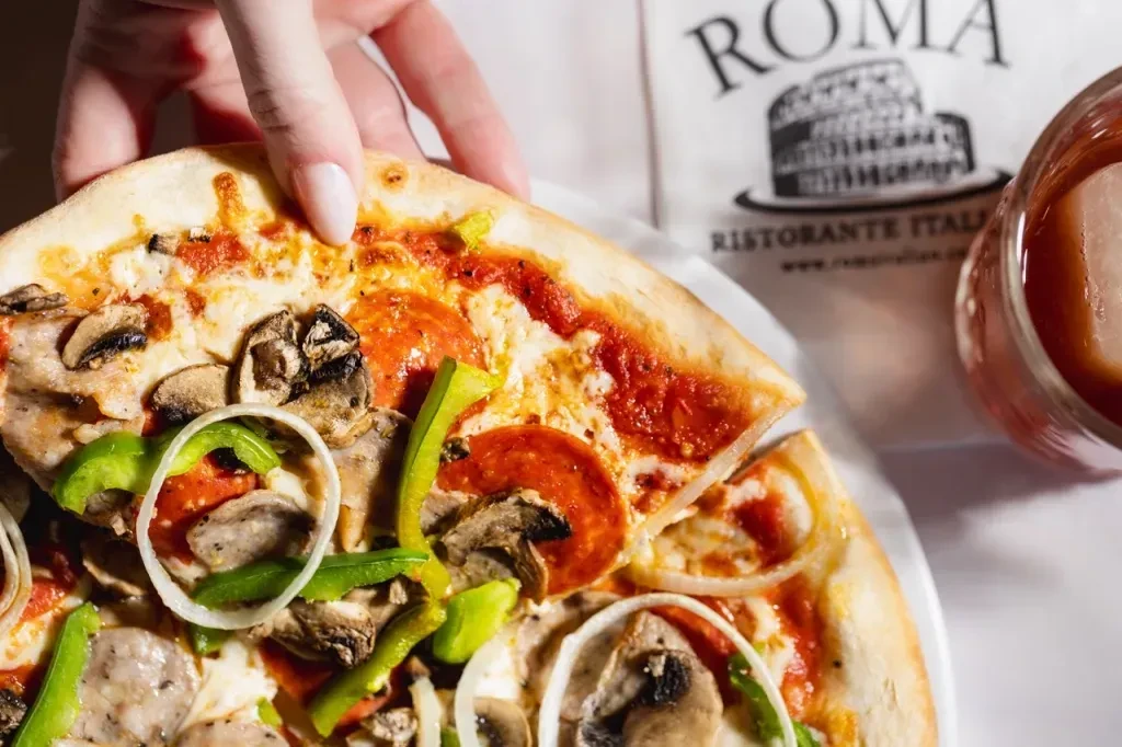 Hand lifting pizza slice with pepperoni, mushrooms, bell peppers.