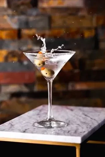 Martini glass with two olives and splashing liquid on marble.