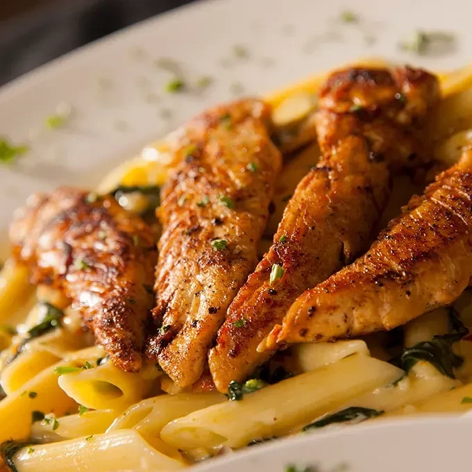 Penne pasta dish with grilled chicken, creamy sauce, and green vegetables.