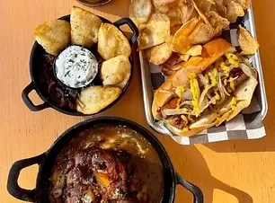 Three pub dishes: fried dumplings, loaded hot dog, and meat stew.