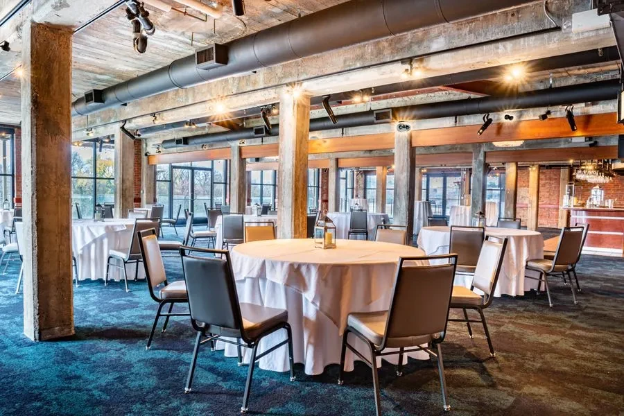 Spacious, empty industrial-chic dining hall with tables, bar, and windows.