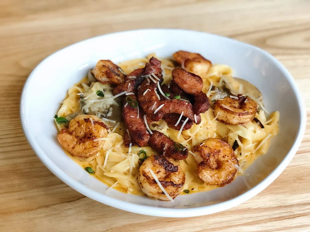 Close-up of creamy pasta with shrimp, sausage, cheese, and green herbs.