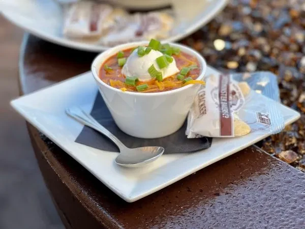 Bowl of hearty soup with cream, cheese, green onions, crackers, spoon.