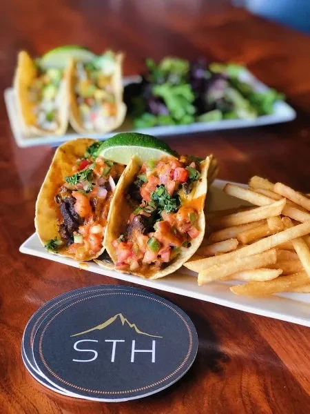 Tacos with meat, salsa, lime, and fries on a white plate.