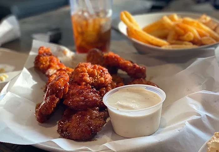 Crispy boneless chicken wings, creamy dip, blurred fries and iced beverage.