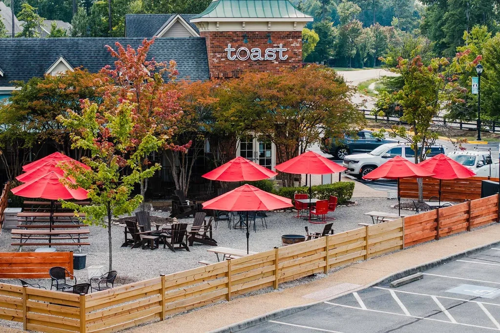 "toast" restaurant exterior with outdoor dining, green roof, and fall trees.