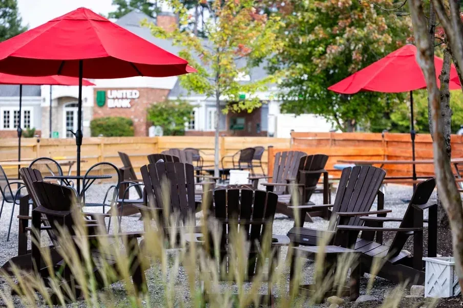 Outdoor patio with Adirondack chairs, red umbrellas, and a bank sign.