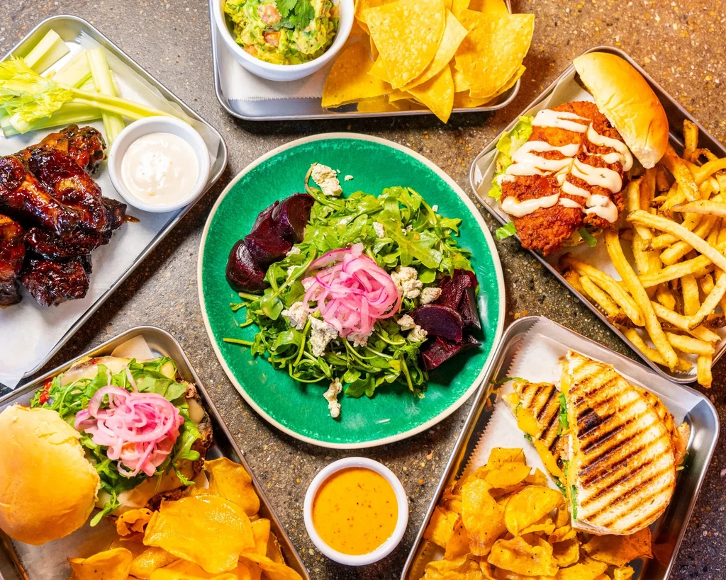 Overhead spread of appetizers, salads, and sandwiches on a dark table.