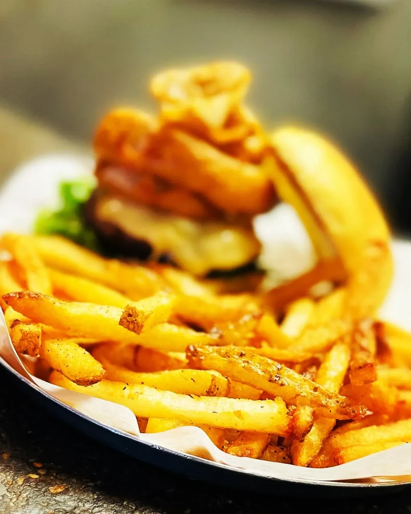 Crispy French fries in focus with a blurred burger and onion rings.