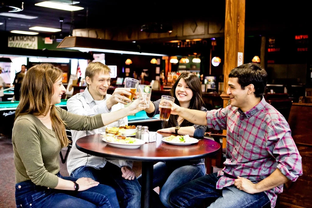Smiling group of four toasting drinks in a lively restaurant bar.