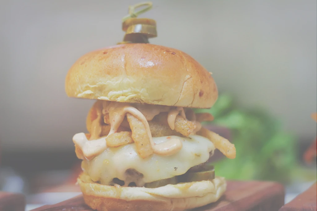 Vertically presented gourmet burger with cheese, sauce, pickles, and jalapeño skewer.