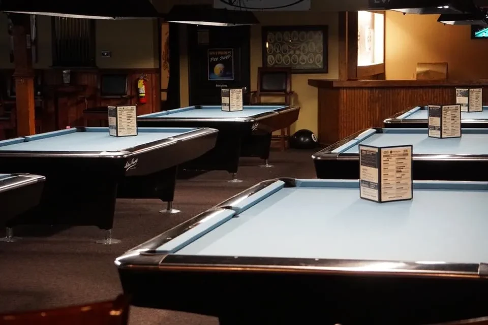 Multiple blue-felt pool tables in a dim, empty billiards hall.