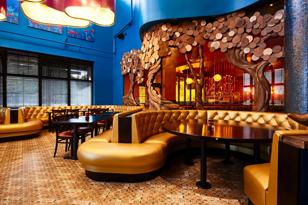 Empty, stylized restaurant with blue walls, golden booths, and disc tree art.