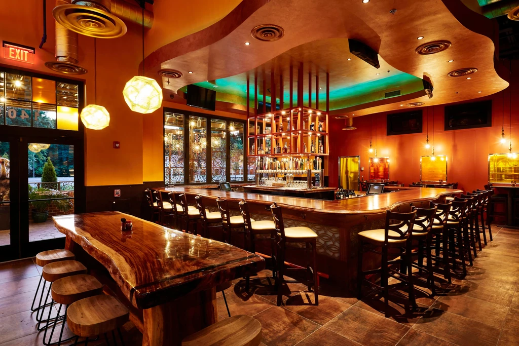 Empty modern bar with live-edge table, curved bar, and green ceiling lights.