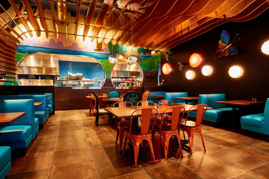 Colorful modern restaurant with teal booths, orange chairs, and open kitchen.