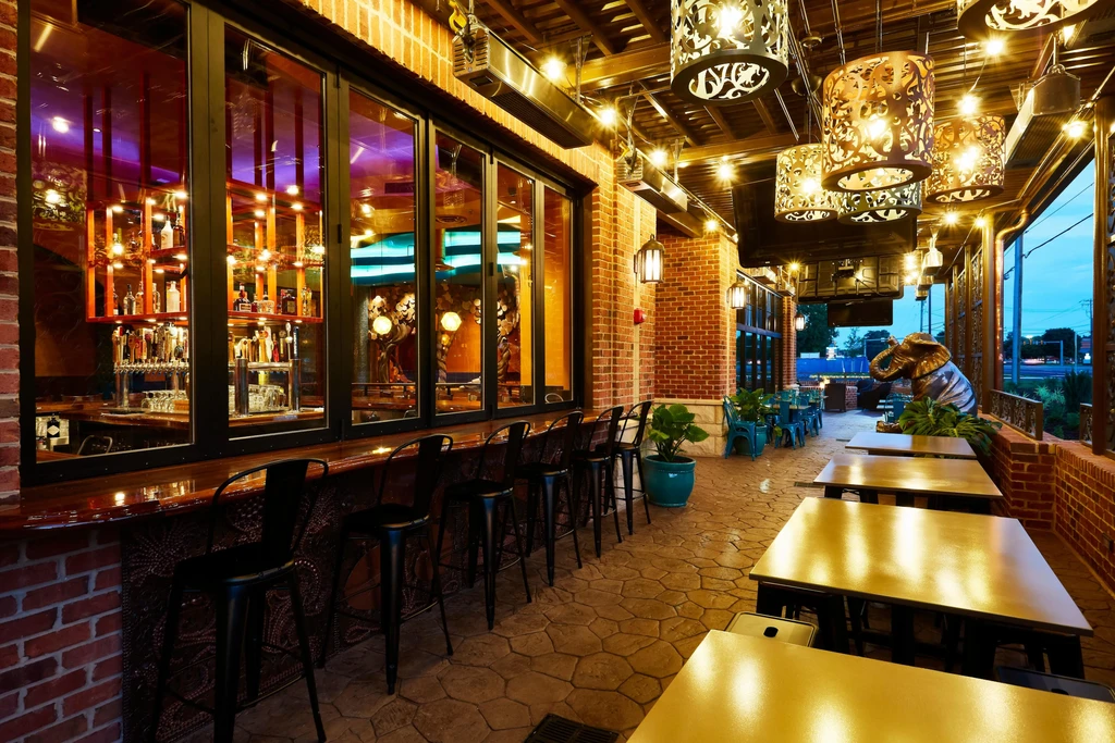 Dusk restaurant patio with string lights, illuminated bar, and elephant statue.