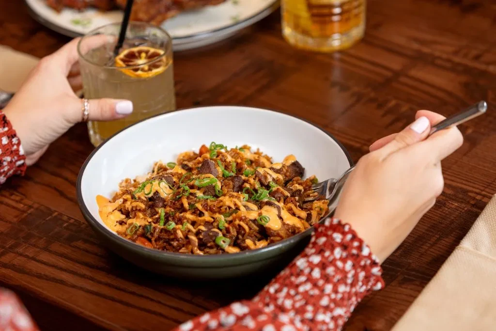 Hands holding fried rice and an orange-garnished drink.