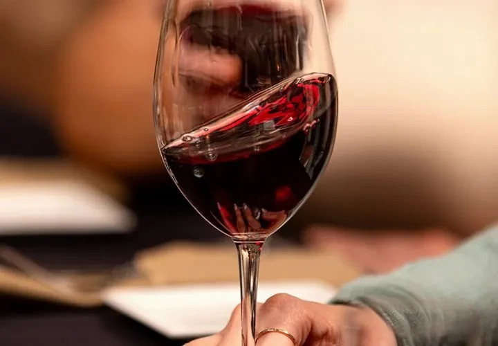 A hand with a gold ring swirls red wine in a glass.