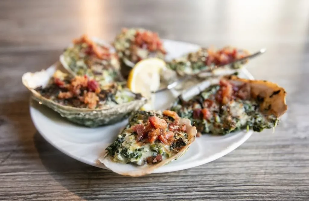 Close-up of six baked oysters topped with green, red, and a lemon.