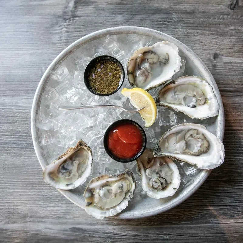 Overhead shot of six shucked oysters on ice with sauces and lemon.