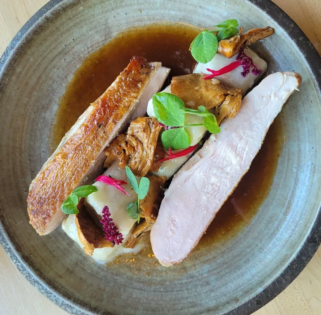 Gourmet crispy-skinned poultry, creamy puree, mushrooms, and edible flowers.