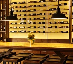 Wine bar interior with backlit display wall, dark counter, and stools.