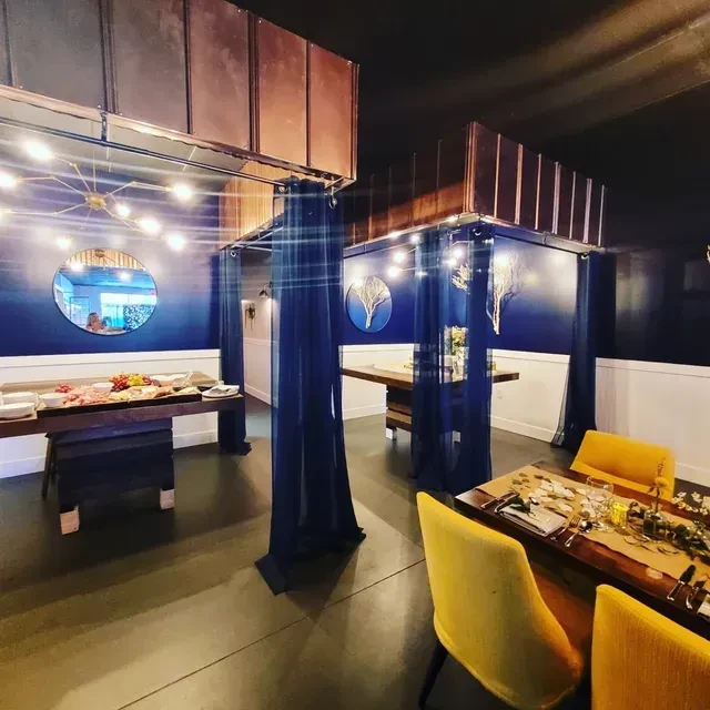 Modern restaurant interior with charcuterie, yellow chairs, blue walls, string lights.