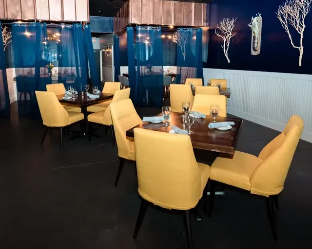Modern restaurant interior with navy walls, mustard chairs, and set tables.