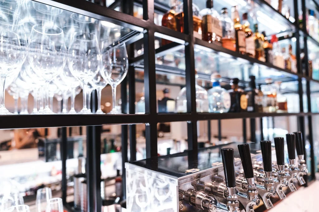 Sleek bar: chrome beer taps, wine glasses, and out-of-focus liquor bottles.